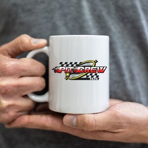 K&ouml;nnte beinhalten: Wei&szlig;e Keramiktasse mit einem schwarz-wei&szlig;en Schachbrettmuster und den Worten "Pit Crew Papa" in roten und gelben Buchstaben.