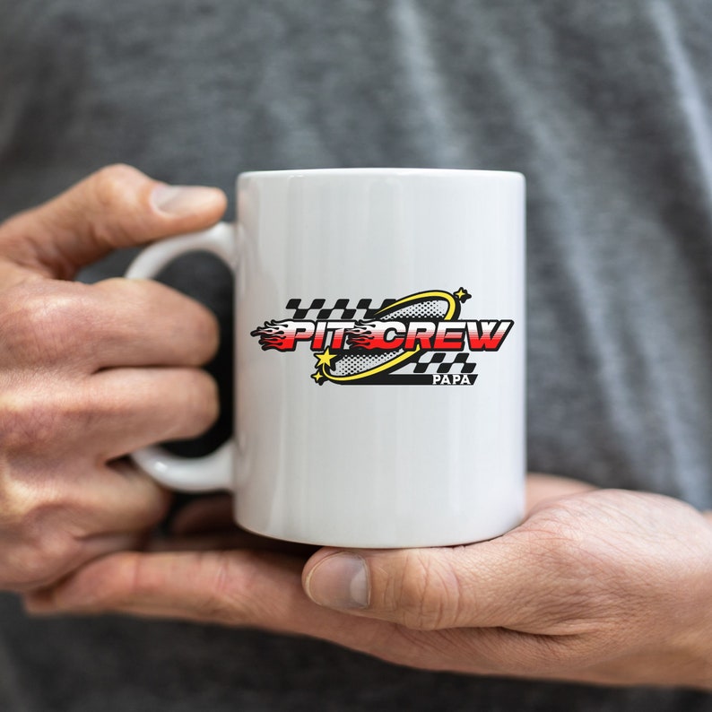 K&ouml;nnte beinhalten: Wei&szlig;e Keramiktasse mit einem schwarz-wei&szlig;en Schachbrettmuster und den Worten "Pit Crew Papa" in roten und gelben Buchstaben.