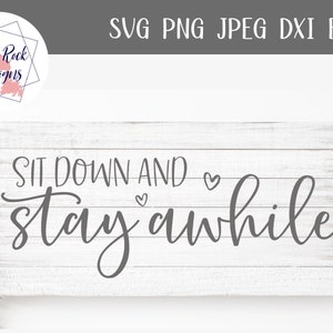 May include: A rectangular wooden sign with the words "SIT DOWN AND stay awhile" in a cursive font. The sign is white with gray text and a heart symbol. The top left corner has a logo.