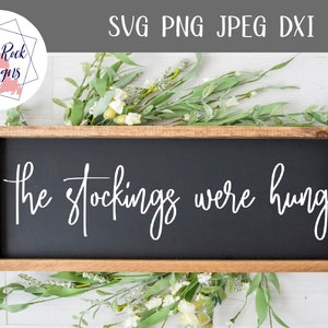 Op de afbeelding: Een houten bord met een zwarte krijtbordachtergrond. Het bord heeft de tekst "The stockings were hung" in witte, cursieve letters.