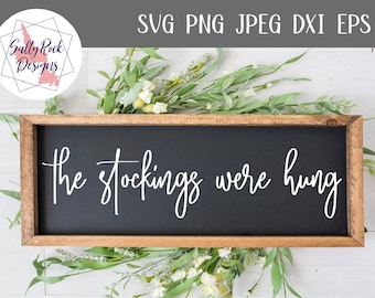Könnte beinhalten: Ein Holzschild mit schwarzem Schiefertafel-Hintergrund. Das Schild trägt die Aufschrift "The stockings were hung" in weißer, kursiv geschriebener Schrift.
