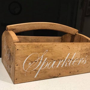 May include: A rustic wooden box with a handle, painted in a light brown colour. The box has the words "Sparkler's" written on the front in white paint.
