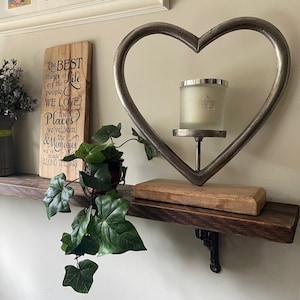 May include: A rustic shelf arrangement featuring a metal heart-shaped candle holder, a wooden sign, and a potted plant. The candle holder, with a silver finish, holds a glass candle. The wooden sign displays the text "The BEST things in life are the people WE LOVE".