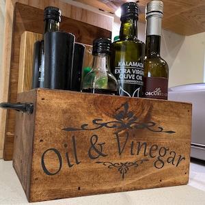 May include: A wooden box with the words "Oil & Vinegar" painted on the front. The box is filled with various bottles of oil and vinegar.