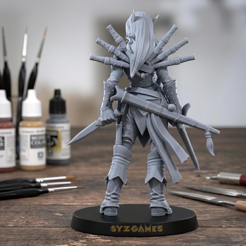 May include: A grey, unpainted miniature warrior figure, holding a sword and a rifle-like weapon. The figure has multiple blades attached to its back. The base reads "SYZ GAMES". Paint bottles and brushes are in the background.