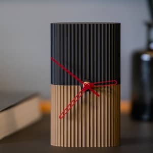 Peut inclure: Une horloge à rayures noires et brunes avec des aiguilles rouges. L'horloge est sur une table avec un livre.