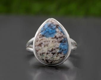 Peut inclure: Une bague en argent avec une pierre bleu et blanc en forme de larme. La pierre a un motif marbré.