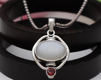 May include: A silver pendant necklace with a white oval gemstone and a small red gemstone. The pendant is set in a silver frame with a delicate design.