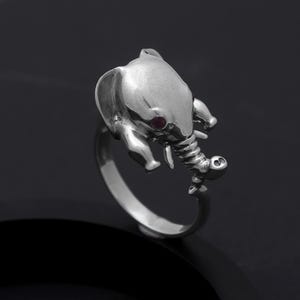 Peut inclure: Une bague en argent avec un motif de tête d'éléphant. L'éléphant a une pierre précieuse rouge pour l'œil.