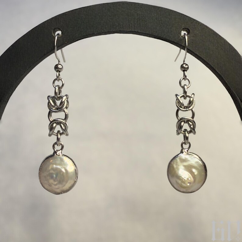 Pode incluir: Um par de brincos de prata com uma gota de p&eacute;rola e um design de corrente.