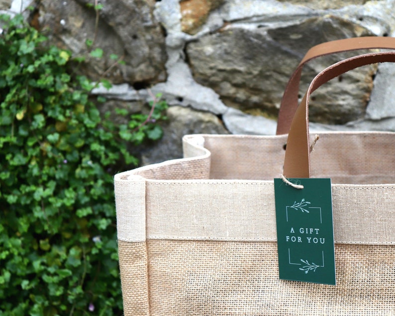 An up-close of our Hessian Market Shopper bag in front of a rustic wall. A green 'Boutique Favours' gift tag is attached.