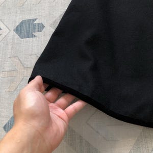 May include: Close-up of the black fabric hem of a garment. The fabric is soft and smooth, with a slight sheen.