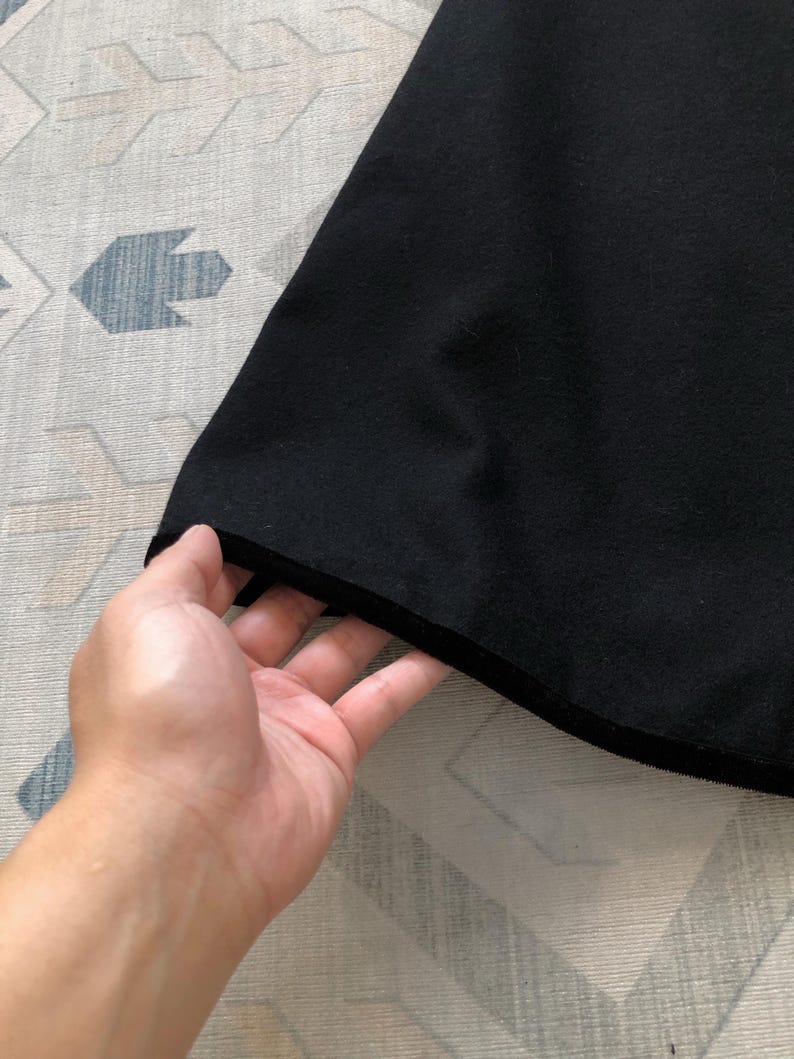 May include: Close-up of the black fabric hem of a garment. The fabric is soft and smooth, with a slight sheen.