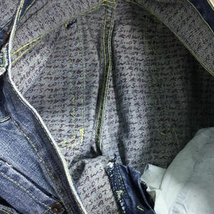 May include: Close-up of the inside of a pair of blue denim jeans. The inside of the waistband is lined with a patterned fabric featuring a repeating design of small, dark brown letters.