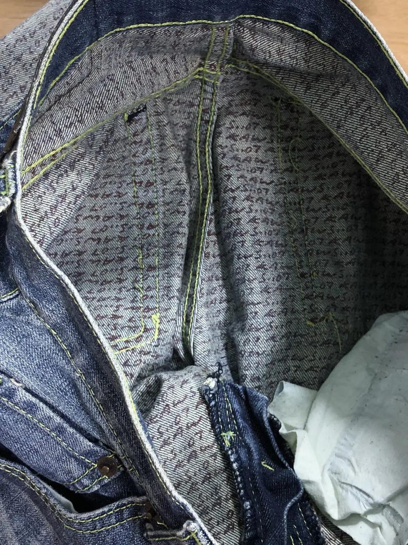 May include: Close-up of the inside of a pair of blue denim jeans. The inside of the waistband is lined with a patterned fabric featuring a repeating design of small, dark brown letters.