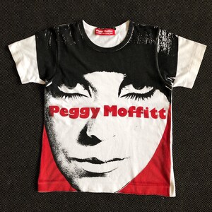 Puede incluir: Camiseta blanca con una imagen en blanco y negro de la cara de una mujer y el texto "Peggy Moffitt" en letras rojas.