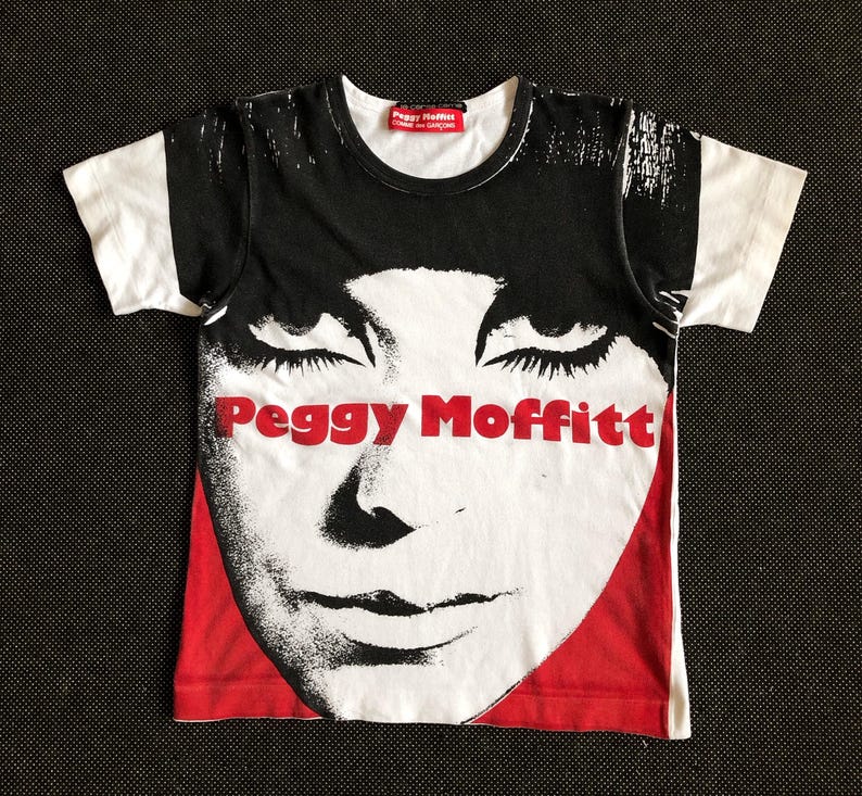 Puede incluir: Camiseta blanca con una imagen en blanco y negro de la cara de una mujer y el texto "Peggy Moffitt" en letras rojas.