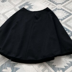 May include: A black, circular skirt with a velvet trim. The skirt is made of a soft, flowing fabric.