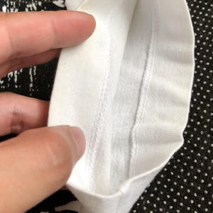 Puede incluir: Primer plano del interior de una camiseta blanca, mostrando las costuras alrededor del cuello.