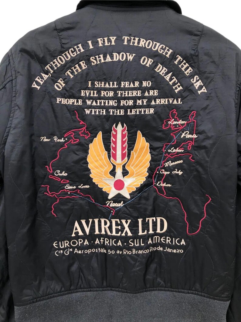Puede incluir: Chaqueta bomber acolchada negra con texto y gr&aacute;ficos bordados. La parte trasera presenta un emblema alado, un mapa y el texto "YEA THOUGH I FLY THROUGH THE SKY OF THE SHADOW OF DEATH". La chaqueta tambi&eacute;n tiene la marca "AVIREX LTD."