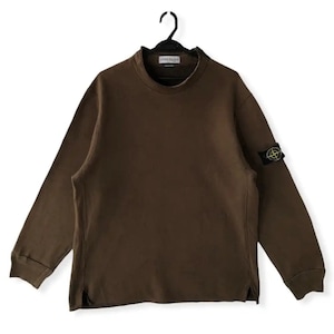 May include: A brown long-sleeved sweatshirt with a mock neck and a Stone Island logo patch on the left sleeve. The logo is a black compass with a yellow centre.