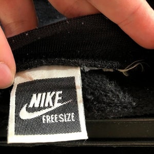 May include: A white tag with black text that reads "NIKE FREE SIZE" on a black sweatshirt.