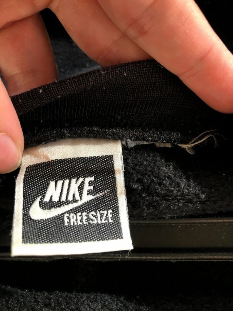 May include: A white tag with black text that reads "NIKE FREE SIZE" on a black sweatshirt.