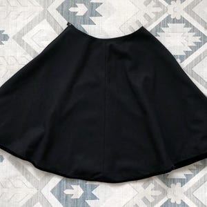 May include: A black circle skirt with a smooth, flowing fabric. The skirt is gathered at the waist and falls to the knee.
