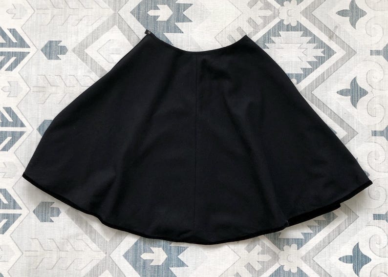 May include: A black circle skirt with a smooth, flowing fabric. The skirt is gathered at the waist and falls to the knee.