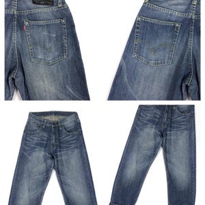 May include: A pair of blue denim jeans with a distressed look. The jeans have a straight leg and a cuffed hem. The jeans have a leather patch on the back with the text "A.X." on it.