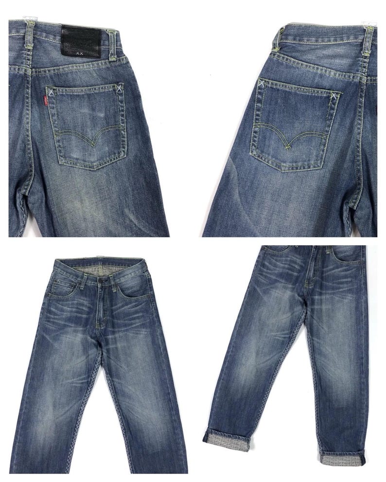 May include: A pair of blue denim jeans with a distressed look. The jeans have a straight leg and a cuffed hem. The jeans have a leather patch on the back with the text "A.X." on it.