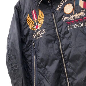 Puede incluir: Chaqueta acolchada azul marino con parches bordados. Presenta los textos "POSTES FRANCE" y "AVIREX EUROPA". Incluye cierre de cremallera y cuello gris. La chaqueta tiene un patr&oacute;n de diamantes.