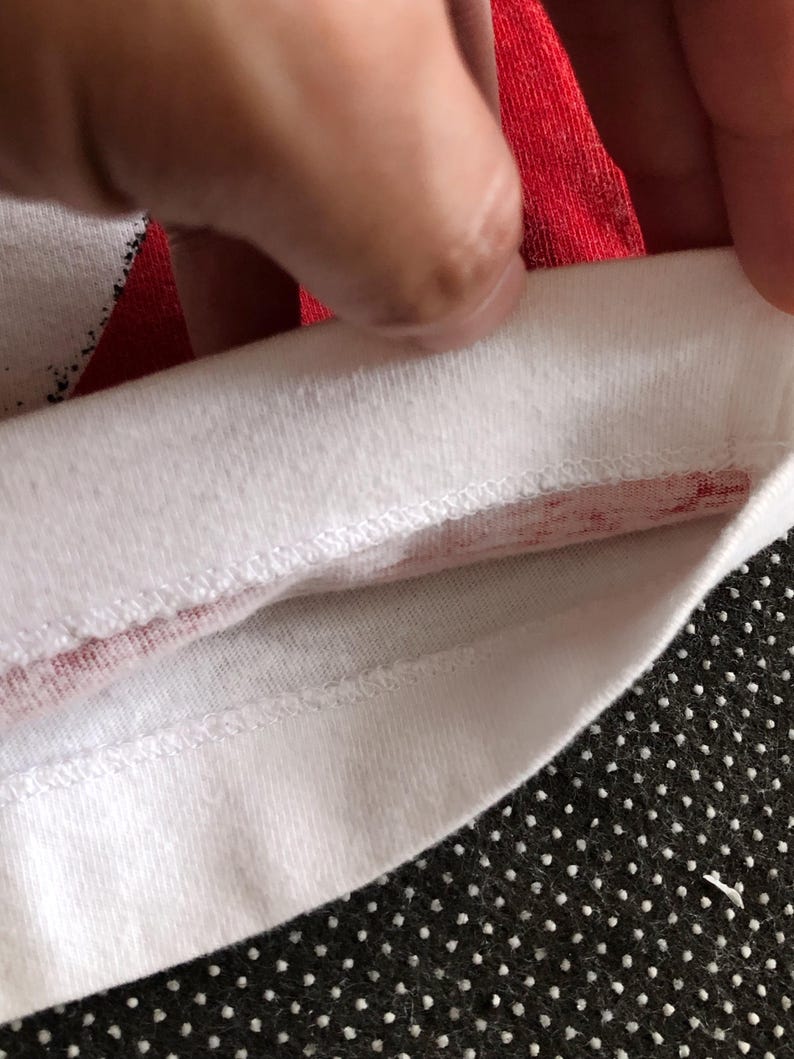 Puede incluir: Primer plano del interior de la costura de una camiseta blanca con una franja roja a lo largo del borde.