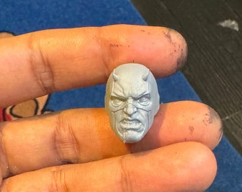 Puede incluir: Una escultura de cabeza de plástico gris de un superhéroe con una máscara roja y una expresión seria. La cabeza mide aproximadamente 5 cm de alto.