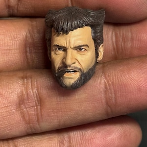 Puede incluir: Una escultura de cabeza detallada de un personaje con cabello castaño, barba y una expresión seria. La escultura está hecha de plástico pintado y está diseñada para usarse con figuras de acción.