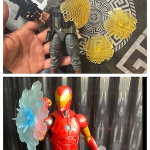 May include: Two action figures, one in a green and black military-style outfit with a honeycomb-patterned shield, and the other in a red and gold suit with a blue and clear shield.