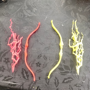 May include: Three 3D printed bows, one red, one yellow and one white. The bows are all different designs, with the red and white bows having a more intricate design than the yellow bow.