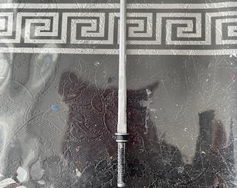 May include: A silver and black toy sword with a black handle. The sword is lying on a black and white patterned surface.