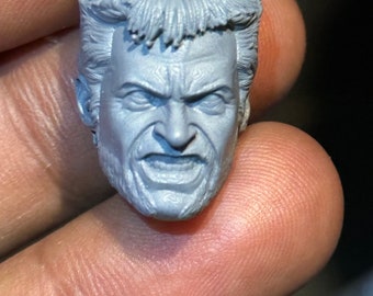 Puede incluir: Una escultura de cabeza de plástico gris de un hombre con el pelo corto y despeinado y el ceño fruncido. La escultura tiene una expresión facial detallada, incluyendo una mueca y el ceño fruncido.