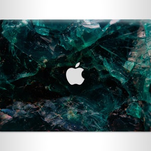 Op de afbeelding: Een laptop met een abstract ontwerp in groen en zwart. Het ontwerp heeft een patroon van gebroken glas of ijs. Het Apple-logo is zichtbaar op de laptop.