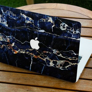 May include: A laptop computer with a black and gold marble design skin. The laptop has a white Apple logo on the lid.