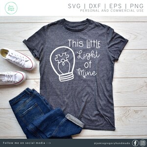 May include: A gray t-shirt with a white outline of a light bulb with a puzzle piece inside. The text "This little Light of Mine" is written in white cursive lettering.