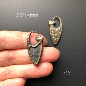 May include: Two antique gold-toned metal cat charms with a detailed design. The charms are 33mm by 14mm and have a textured finish. The charms are on a black background.