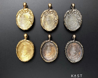 Könnte beinhalten: Sechs ovale Anhänger-Rohlinge mit einem dekorativen floralen Rand. Die Rohlinge sind aus Metall und in drei Ausführungen erhältlich: Gold, Silber und Antikmessing. Die Rohlinge sind in zwei Reihen zu je drei angeordnet, wobei die goldenen Rohlinge in der mittleren Reihe liegen.