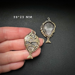 May include: Two gold-tone metal fish pendant charms, one with a detailed design and the other with a blank oval space for a stone or cameo. The charms measure 39 x 23 mm.