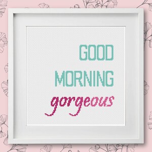 May include: White framed cross-stitch with the text "GOOD MORNING gorgeous" in teal and pink.