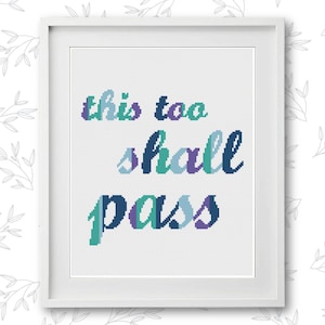 Puede incluir: Bordado de punto de cruz enmarcado en blanco con la frase "This too shall pass" en letras azules, verdes y moradas.
