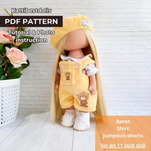 May include: PDF pattern for a 11 inch doll outfit. The outfit includes a yellow beret, a white shirt, and yellow overalls with a brown bear design. The doll has long blonde hair.