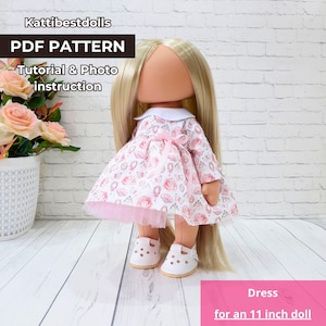 May include: PDF pattern for a dress for an 11 inch doll. The dress is pink with a floral print and a white collar. The doll has long blonde hair and is wearing white shoes.