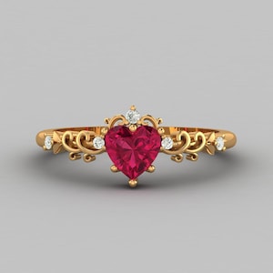 May include: A gold ring with a heart-shaped ruby gemstone surrounded by smaller diamonds. The ring features a delicate, ornate design with scrolling details.